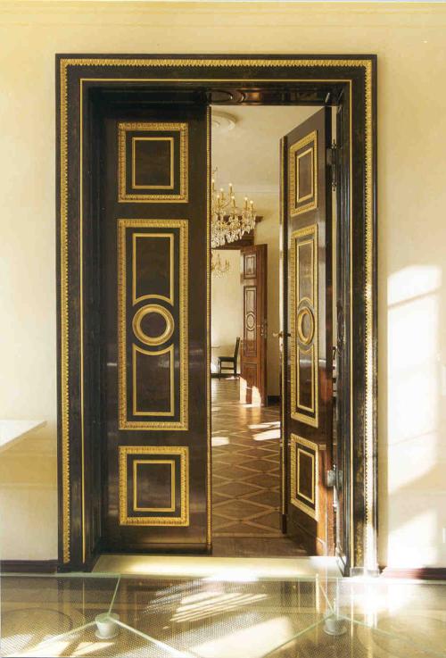 Geöffnete hohe dunkle Holztür mit goldenen Kassetten-Verzierungen in einem Schloss